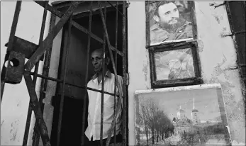  ?? Enrique de la Osa, Reuters ?? A man stands inside his house near a photograph of former Cuban President Fidel Castro
and rebel revolution­ary commander Camilo Cienfuegos in Havana on Saturday.