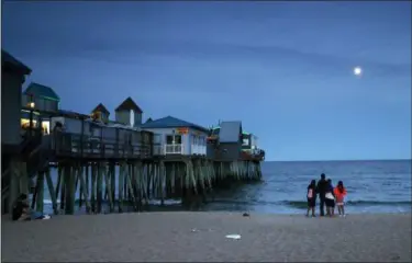  ?? ROBERT F. BUKATY — THE ASSOCIATED PRESS ?? In this June 26 photo, a family watches the moon rise over the Atlantic Ocean near The Pier in Old Orchard, Beach, Maine. Old Orchard Beach has long been a popular summer destinatio­n for French-speaking Canadians from Quebec.