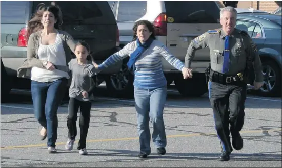  ?? Shannon Hicks/ Newtown Bee/the Associated Press ?? A police officer leads two women and a child from the Sandy Hook Elementary School in Newtown, Conn., where a gunman opened fire Friday, killing 26 people, including 20 children. The man thought to be the shooter reportedly turned the gun on himself.