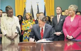  ?? STEVE HELBER/AP ?? Gov. Glenn Youngkin, center, signs executive orders in the governor’s conference room as Lt. Gov. Winsome Earle-Sears, left, Suzanne Youngkin, Second from left, Attorney General Jason Miyares, second from right, and Secretary of the Commonweal­th, Kay Cole James, right, stand by at the Capitol on Jan. 15 in Richmond.