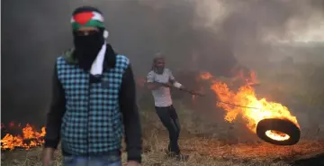  ??  ?? A Palestinia­n protester moves a burning tire during clashes with Israeli troops at Israel-Gaza border, in the southern Gaza Strip. — Reuters photo