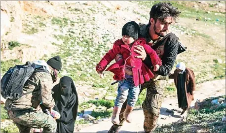  ?? FADEL SENNA/AFP ?? A fighter with the Syrian Democratic Forces (SDF) helps women and their children on a field after they fled from the Baghouz area in Syria’s Deir Ezzor on Tuesday during an operation to expel hundreds of Islamic State group (IS) jihadists from the region.