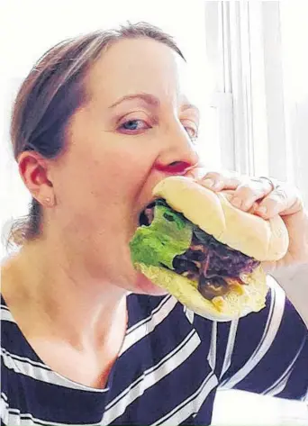  ??  ?? Jill Forse digs into a burger at the Port Pub in Port Williams, Nova Scotia as part of the Annapolis Valley’s Burger Wars, which is held each April as a fundraiser for Campaign for Kids.