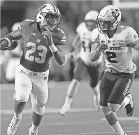  ?? MARK HOFFMAN / MILWAUKEE JOURNAL SENTINEL ?? Wisconsin running back Jonathan Taylor rumbles for a first down while being pursued by Utah State’s Dallin Levitt on Friday night.