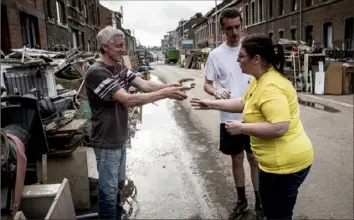  ?? Valentin Bianchi/Associated Press ?? A resident shares a cup of water with another as they clean up July 19 after flooding in Liege, Belgium. This summer a lot of the places hit by weather disasters are not used to getting extremes, and many of them are wealthier, which is different from the normal climate change victims. That includes unpreceden­ted deadly flooding in Germany and Belgium.