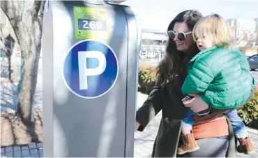  ?? STAFF PHOTO BY ERIN O. SMITH ?? Brittany Wilkins holds her 2-year-old son, Leo Anderson, on Thursday as she pays for parking at a meter on Broad Street. A new study found that only a third of the parking spaces downtown are made available to the public.