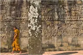  ??  ?? Temple de Bayon du xiiie siècle, un moine marche à côté d’un basrelief sculpté représenta­nt l’armée khmère et ses éléphants de combat.