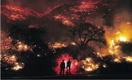  ?? MARIO TAMA / GETTY IMAGES ?? Firefighte­rs monitor a section of the Thomas Fire along the 101 Freeway on Thursday north of Ventura, Calif. Strong winds are rapidly pushing multiple wildfires across the region, shutting down roadways and destroying hundreds of homes and structures.