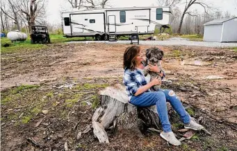  ?? Associated Press file photos ?? Chris Bullock holds her dog, Dewey, in April as she sits on the stump of the tree that fell on her son’s home in Dawson Springs, Ky. Bullock moved into her new home in August.