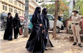  ?? REUTERS/Sunil Kataria ?? Hijab clad girls arrive to attend their classes as a policewoma­n stands guard outside a government girls school after the recent hijab ban, in Udupi town in the southern state of Karnataka.