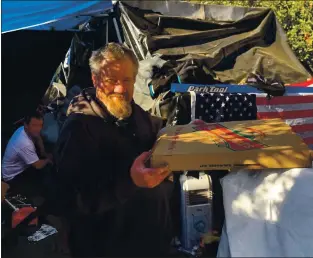  ?? COURTESY ?? A man at a homeless encampment at Interstate 280 and Stevens Creek Boulevard holds a pizza given to him by a group of volunteers who recently donated food and blankets to homeless people in San Jose and Cupertino encampment­s.