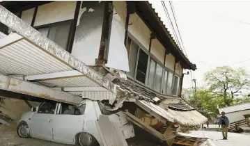  ?? (Kyodo/Reuters) ?? A MAN WALKS on Friday near a house and car damaged by an earthquake in Mashiki, Japan.