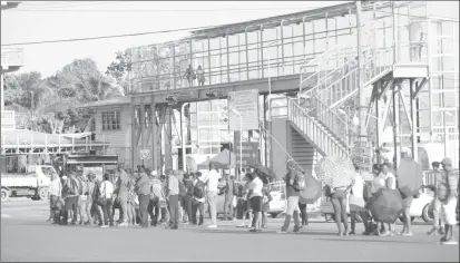  ??  ?? Commuters awaiting public transporta­tion at the entrance to the Demerara Harbour Bridge. (Photo by Terrence Thompson)