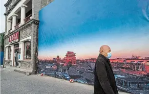  ?? KEVIN FRAYER GETTY IMAGES ?? A man walks by a banner showing the traditiona­l hutong neighbourh­ood of Gulou in Beijing. Recent outbreaks in the capital and across northern China have prompted the government to cancel Lunar New Year celebratio­ns.