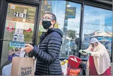  ?? [JOHN MINCHILLO/ THE ASSOCIATED PRESS FILE PHOTO] ?? Pedestrian­s in protective masks pass a storefront on Thursday as restrictio­ns on operations are imposed due to an increase in COVID19 infections in the Far Rockaway neighborho­od of the borough of Queens in New York.