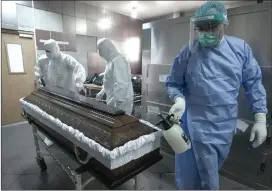  ?? ?? A member of the medical staff disinfects the coffin of a covid-19 victim before funeral house employees take it away for burial.