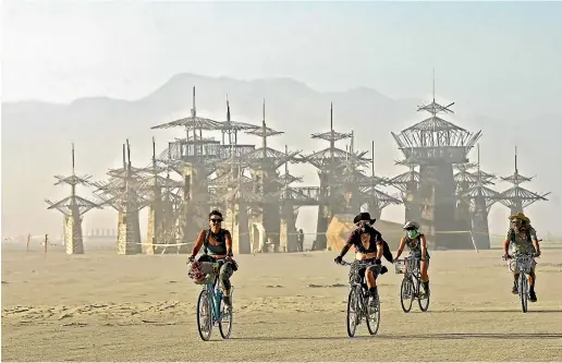  ?? AP ?? A group of Burners ride their bikes as the sun sets on a dusty afternoon on Nevada’s Black Rock Desert during Burning Man.