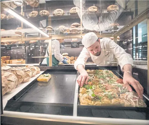  ?? PHOTOS BY BLOOMBERG ?? A baker places a tray of focaccia breads into the display cabinet in the roastery and bake hall at Harrods in London.