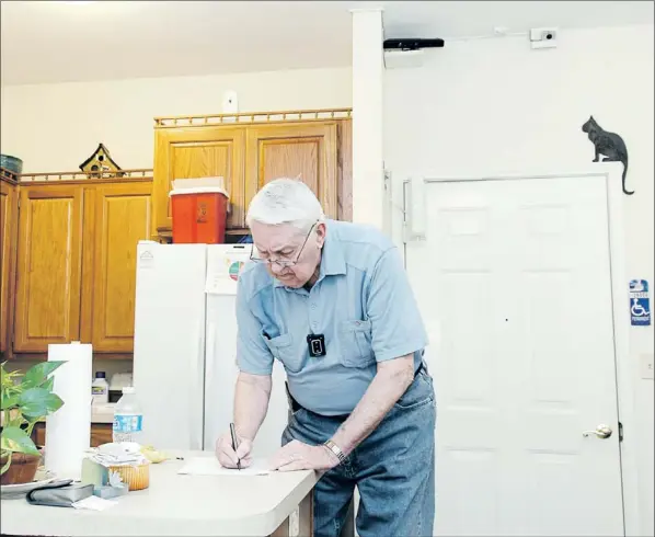  ?? — Photo courtesy of the University of Missouri ?? Bob Harrison writes in his apartment in Columbia, Mo., as different sensors mounted near the ceiling record his activity patterns.