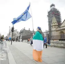  ??  ?? An anti-brexit protester draped in an Irish tricolour flag and holding an EU flag demonstrat­es outside of the Houses of Parliament in London.