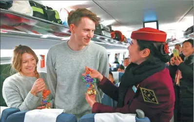  ?? ZOU HONG / CHINA DAILY ?? Rasmus Larsen (center) and Dea Nielsen from Switzerlan­d, who are on a trip to Yunnan province, get presents from the chief conductor of a train at Beijing West Railway station on Friday. The Spring Festival travel rush started on Friday as hundreds of...