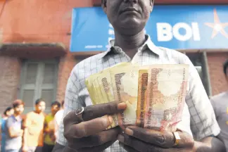 ??  ?? An Indian bank customer counts old rupee notes as he waits outside a bank to deposit and exchange them in Kolkata, last year.