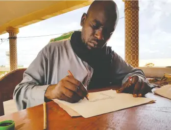  ??  ?? Calligraph­er Boubacar Sadeck finds some shade from the Sahara sun to work on a custom order.