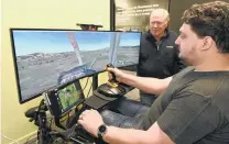  ?? PHOTO: LINDA ROBERTSON ?? Ready for takeoff . . . TracMap technical product owner Tim Neumegen (foreground) demonstrat­es the new TracMap TMLA GPS unit for agricultur­al pilots on a flight simulator at the company’s premises in Mosgiel as aviation sales manager Gerald Harrex looks on.