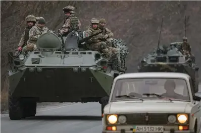  ?? The Associated Press ?? ■ Ukrainian servicemen sit atop armored personnel carriers driving on a road Thursday in the Donetsk region, eastern Ukraine. Russian President Vladimir Putin on Thursday announced a military operation in Ukraine and warned other countries that any attempt to interfere with the Russian action would lead to “consequenc­es you have never seen.”