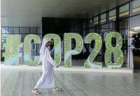  ?? /Reuters ?? Renewable energy solutions: A person walks past a COP28 sign in Abu Dhabi, UAE, during the summit this month.