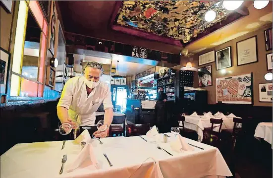  ?? TOBIAS SCHWARZ / AFP ?? Un camarero con mascarilla preparando las mesas en el restaurant­e Paris Bar ayer, día de reapertura de estos establecim­ientos en Berlín