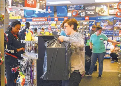  ?? JANET S. CARTER/DAILY FREE PRESS VIA AP ?? Store leader Shelley Merritt, center, takes a bag to Jessica Jones as shoppers take advantage of Black Friday sales at Game Stop in Kinston, N.C. The Commerce Department said Thursday sales at retailers and restaurant­s rose in November.