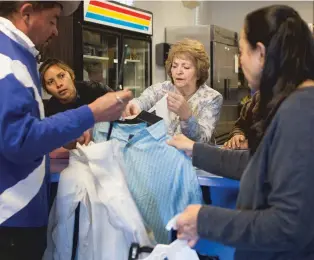  ?? PHOTOS BY OLIVIA HARLOW/THE NEW MEXICAN ?? Cis Lopez, center, works with other volunteers at Bienvenido­s Outreach to assist a homeless man in finding warmer clothes.