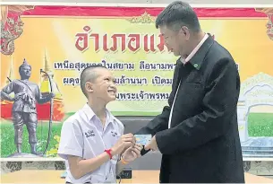  ?? CHIANG RAI PUBLIC RELATIONS OFFICE VIA EPA ?? Mongkol Boonpiam, left, one of the four Wild Boars football team members who have officially received Thai citizenshi­p, smiles as he receives a citizen ID card from Mae Sai district chief Somsak Kanakham on Wednesday.