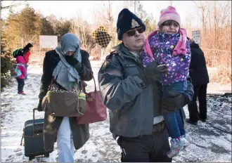  ?? The Canadian Press ?? An RCMP officer escorts a woman and a child claiming to be from Yemen as they cross the U.S.-Canada border in Hemmingfor­d, Que., Sunday.