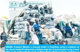  ?? —AFP photos ?? HARARE: Prudence Mkonyo, a charcoal vendor in Zimbabwe, serves a customer as she stands beside 50-kilogramme polythene bags full of charcoal piled on top of each other as she openly sells her wares at Mbare Musika Market in Harare. Zimbabwe is losing more than 330,000 hectares of forest annually. Agricultur­e is still the number one driver of deforestat­ion.