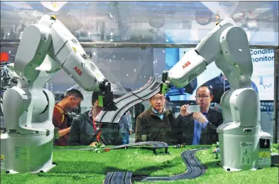  ?? LONG WEI / FOR CHINA DAILY ?? Visitors watch ABB robots build a model at an exhibition in Shanghai.
