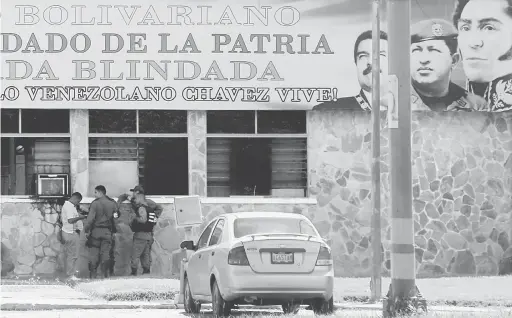  ?? — Gambar Reuters ?? TERKAWAL: Anggota pasukan keselamata­n berdiri di bawah papan tanda yang memaparkan potret (dari kiri) Maduro, bekas presiden Hugo Chavez dan hero negara Simon Bolivar di luar pangkalan tentera 41 Brigada Blindada Fuerte Paramacay di Valencia, kelmarin.