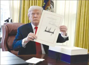  ?? AP PHOTO ?? President Donald Trump displays the US$1.5-trillion tax overhaul package he signed in the Oval Office of the White House in Washington. Trump touted the size of the tax cut, declaring to reporters in the Oval Office before he signed it Friday that “the...