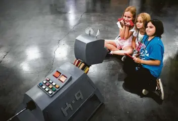  ?? Marie D. De Jesús / Staff photograph­er ?? Ava Harris, 8, from left, Lillian Harris, 5, and Cora Vrubel, 8, squeeze together for a photo taken by Doctor Who’s robotic companion, K9, at the Houston Maker Faire at the George R. Brown Convention Center.