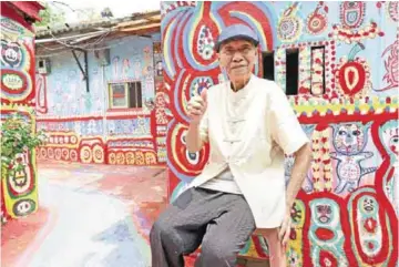  ??  ?? Huang Yung-fu posing for a photo next to his artwork in the Rainbow Village.