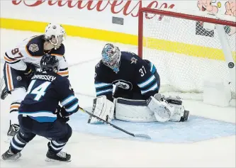  ?? TREVOR HAGAN THE CANADIAN PRESS ?? Edmonton Oilers’ Connor McDavid (97) scores on Jets goaltender Connor Hellebuyck with Josh Morrissey trailing during National Hockey League action in Winnipeg on Tuesday. The Oilers won, 5-4 in overtime.