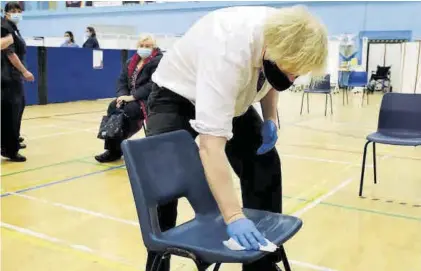  ??  ?? Boris Johnson desinfecta una silla en un centro de vacunación, ayer.