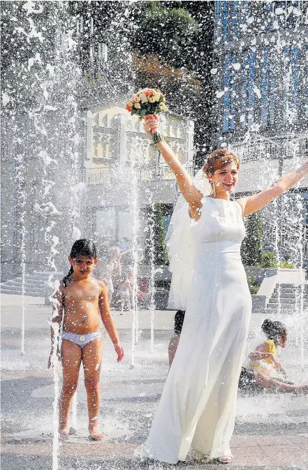  ??  ?? A bride joins children cooling off in a fountain as heatwave conditions engulf Kiev in Ukraine. At least five people have died from the extreme conditions in