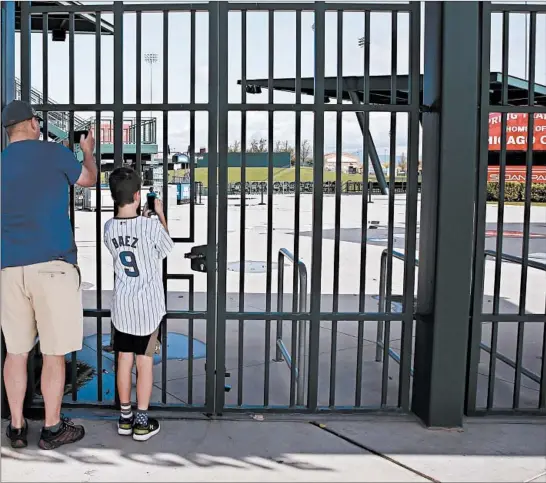  ?? SUE OGROCKI/AP ?? Cubs fans take photos through the gates on Friday at Sloan Park, the spring training site of the Cubs. MLB has suspended the rest of its spring training schedule due to the coronaviru­s.