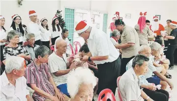  ??  ?? Yii (standing front) presents Christmas goodies to the senior citizens at Home for the Aged. Lukanisman is on his right.