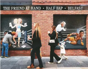 ?? ?? 北愛爾蘭的貝爾法斯特，人們走過藝術家 Ciaran Gallagher(左) 的一幅壁畫，這壁畫反映英國首相特­拉斯惹出的政治麻煩。 （美聯社）