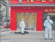 ?? AFP ?? ■
Officials in protective suits stand next a grey-haired man wearing a mask who collapsed and died on a street near a hospital in Wuhan on Thursday. An AFP journalist at the site said that the man, who still had a plastic shopping bag in his hand, was initially moving, but the few passers-by there dared not go near him.