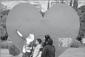  ?? AP/HASSAN AMMAR ?? A Syrian girl takes a selfie Wednesday with her family at a Damascus sculpture meant to show love for the war-torn nation’s capital.