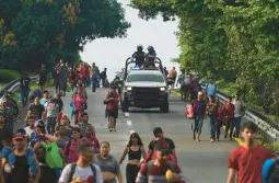  ?? MARCO UGARTE/AP ?? Members of the Mexican National Guard drive alongside migrants Thursday headed toward Huixtla, Mexico. Venezuelan­s make up a large proportion of the caravan.